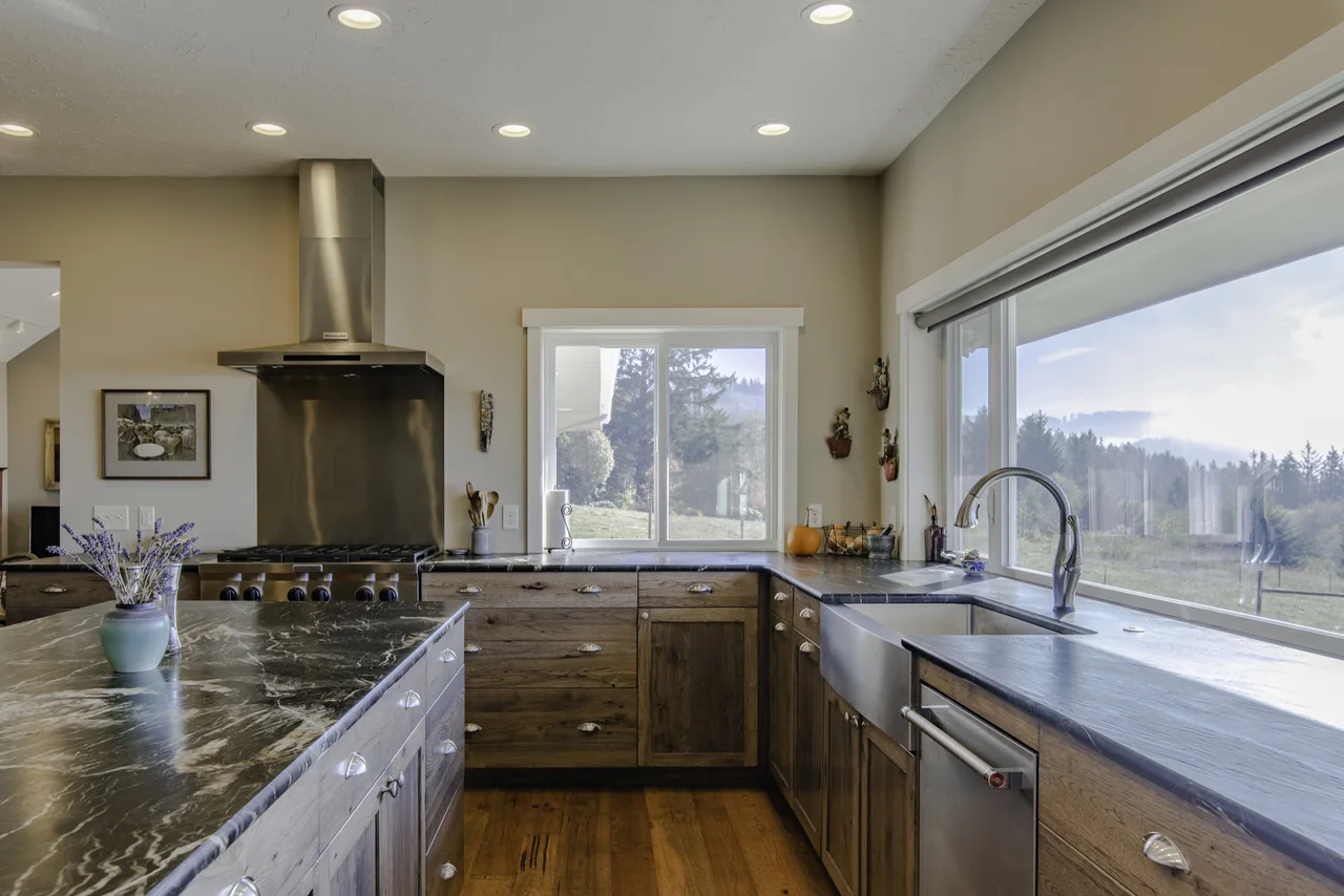 Warm-grain kitchen cabinetry around a range, sink, and stone-topped island